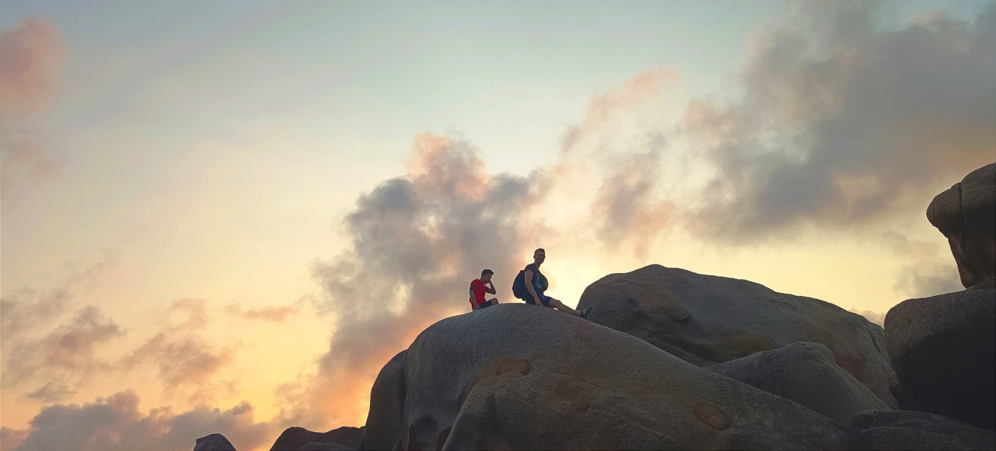 Adam und Ba sitzen auf einem Felsen am Strand in Ke Ga in Vietnam. Man sieht einen wunderschönen Sonnenaufgang