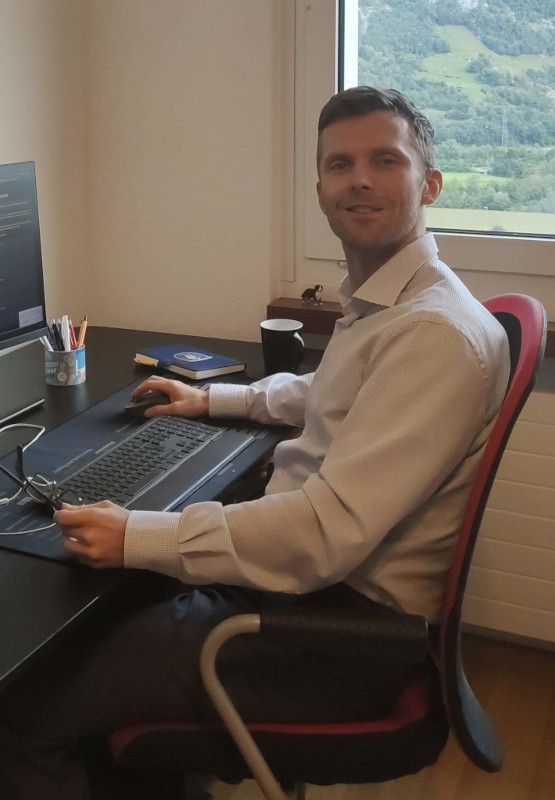 Adam sitzt am Schreibtisch mit Brille in der Hand und analysiert Softwarearchitekturen